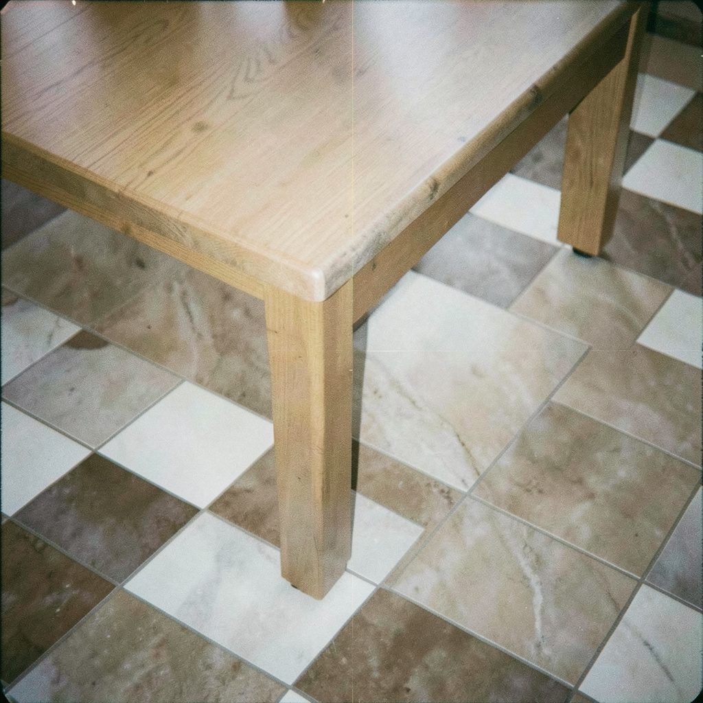 Dim, grainy film photograph of a simple wooden dining table on light floorboards, evoking a steady, disciplined training space