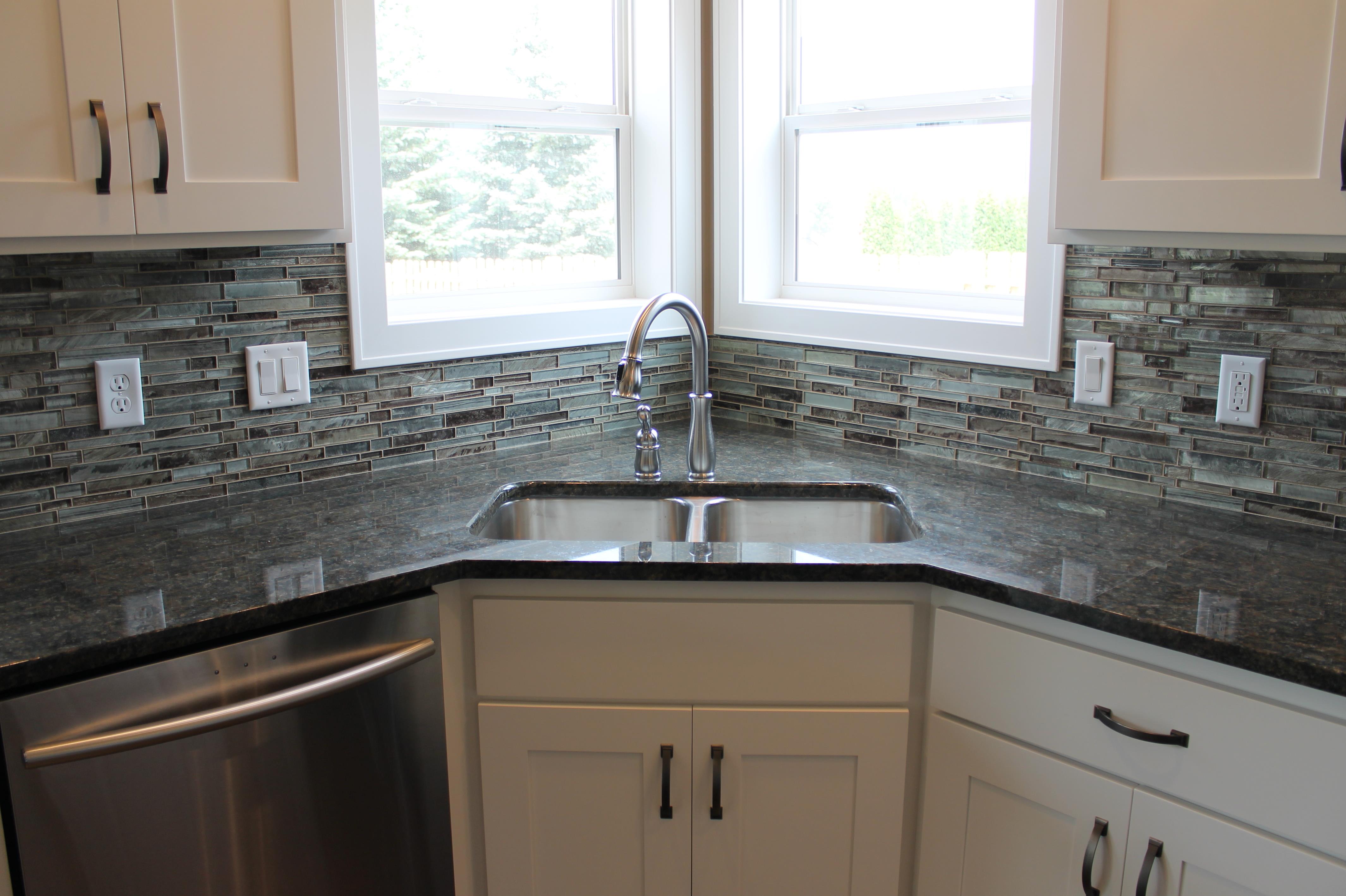 Analog film photograph of a clean kitchen workspace with dark granite, white cabinetry, and a stainless sink, softly lit with visible film grain